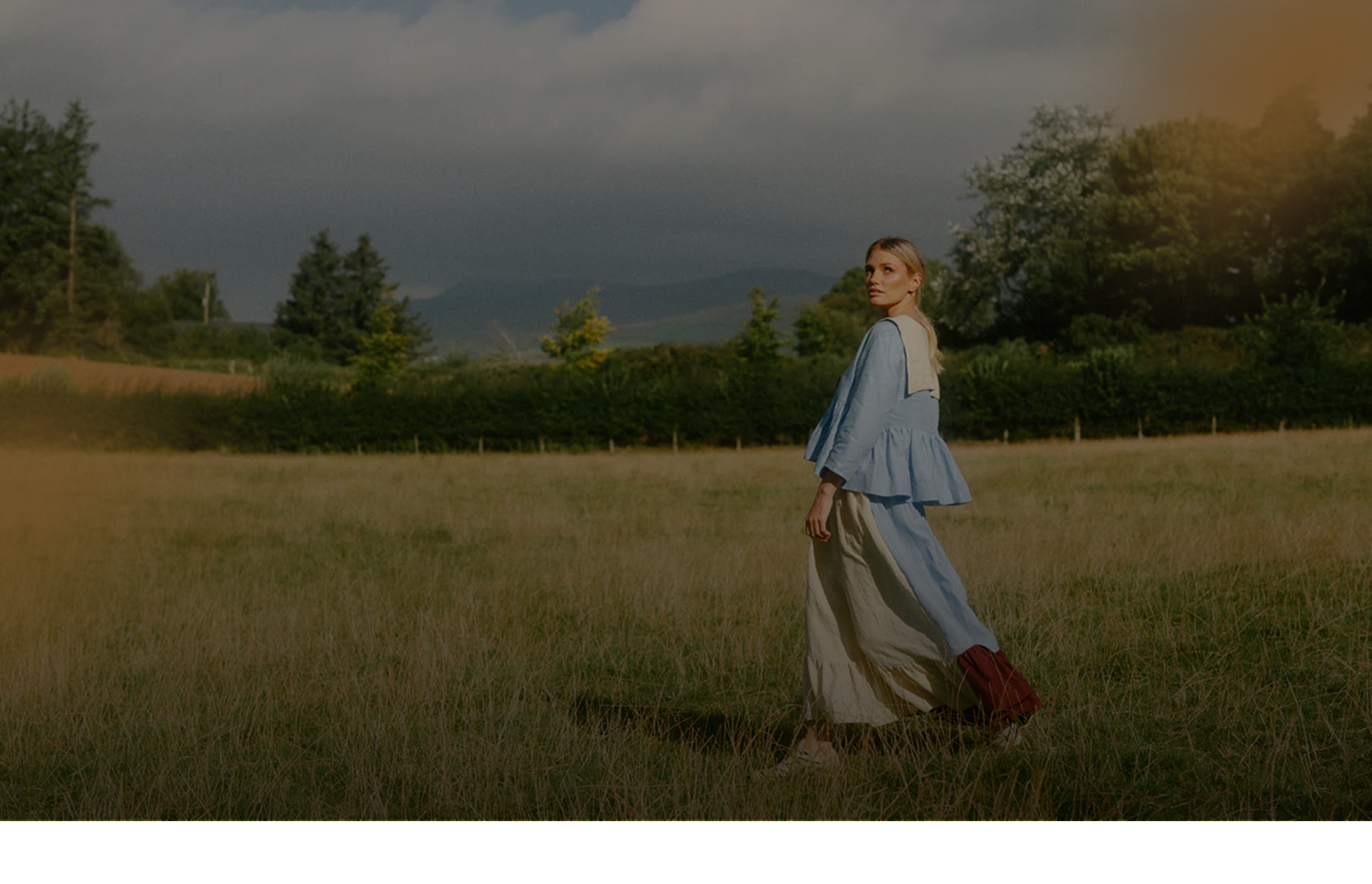 Woman in a blue linen dress walking through a meadow at dusk